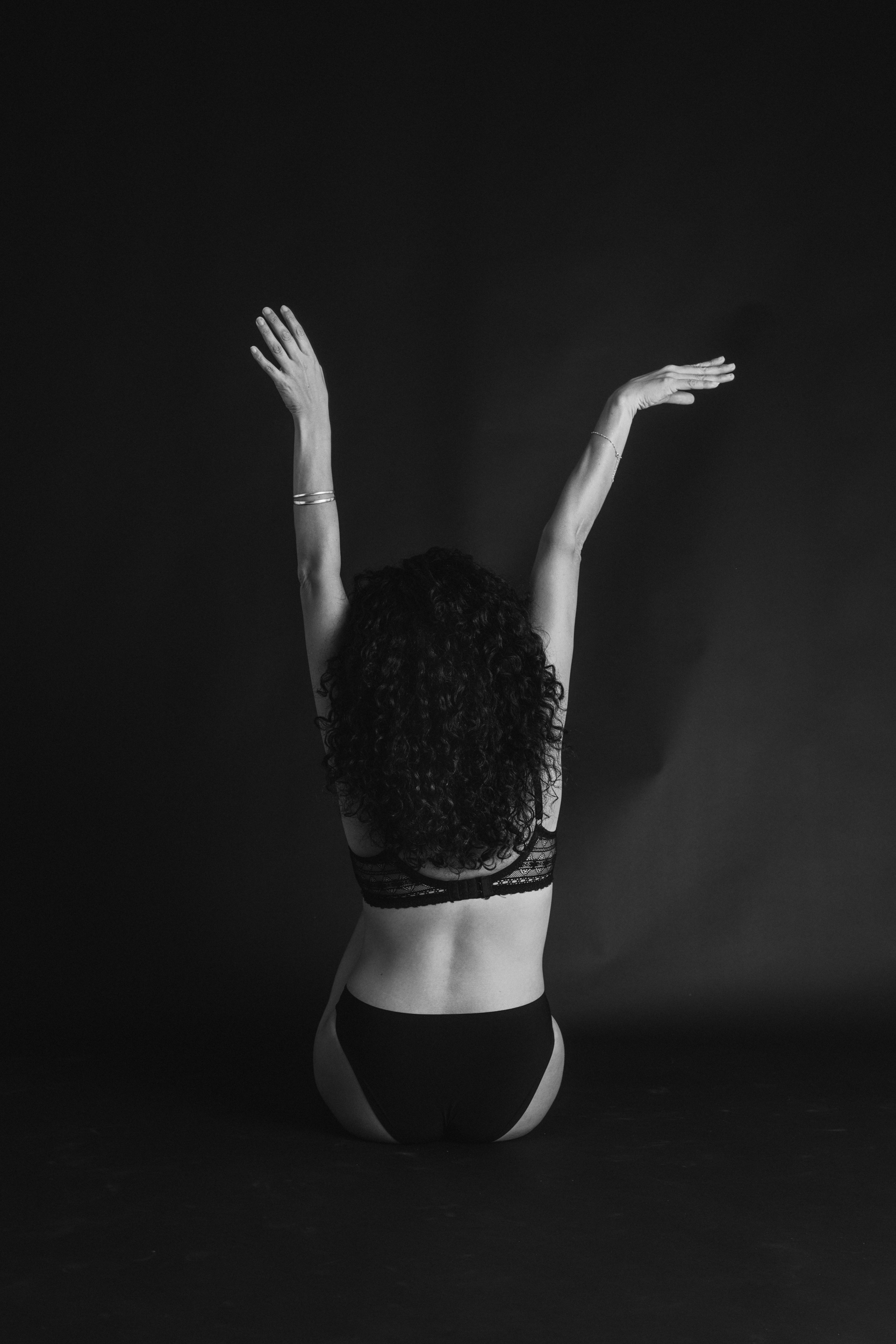 Black and white fine art intimate boudoir photography; woman in underwear from behind stretching arms up 