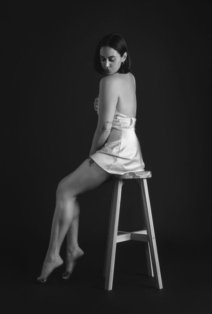 Black and white intimate boudoir pohtography, woman on stool in silk dress