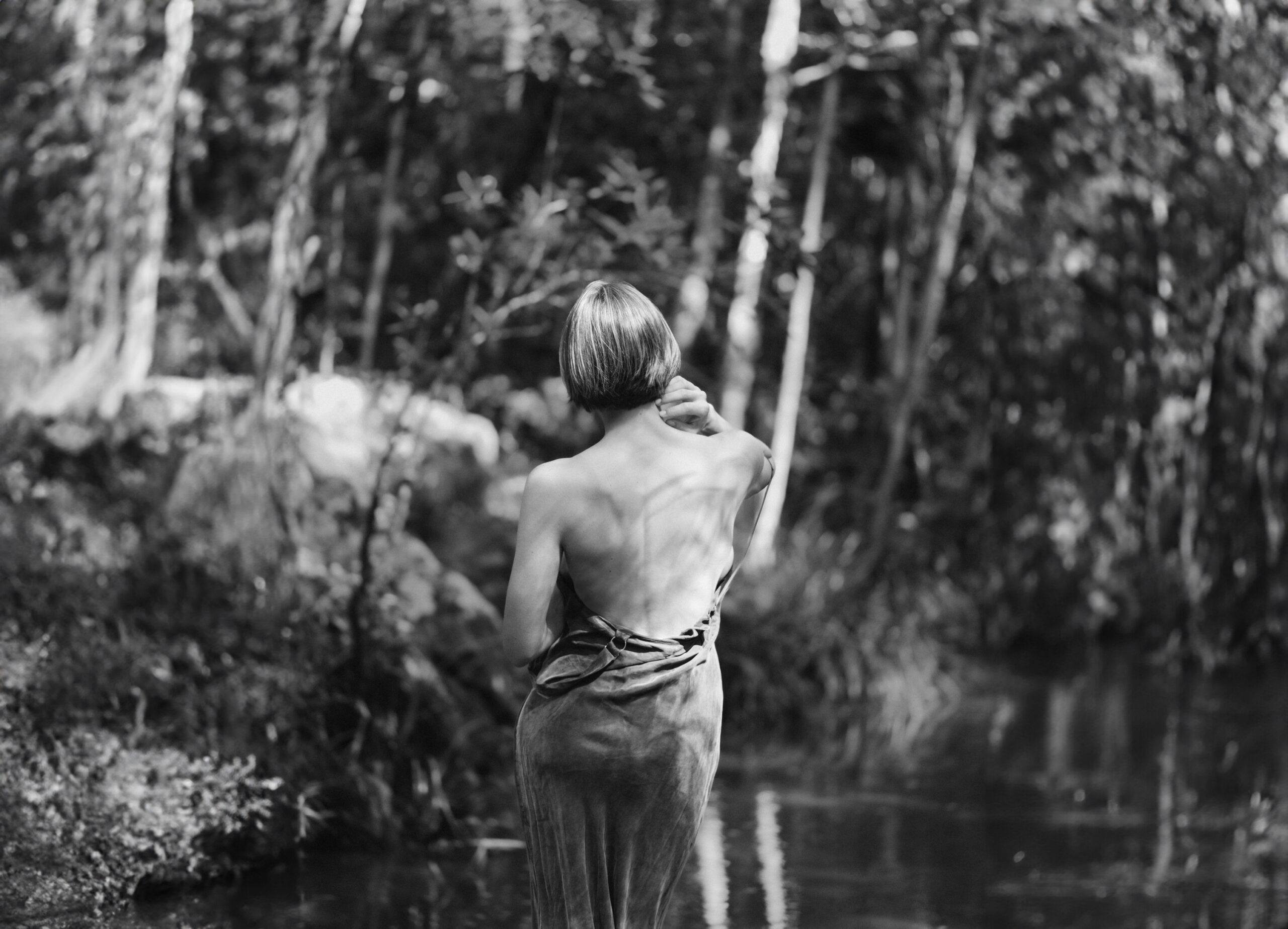 Beautiful woman with a bare back in a natural forest setting; lack and white intimate boudoir photograph